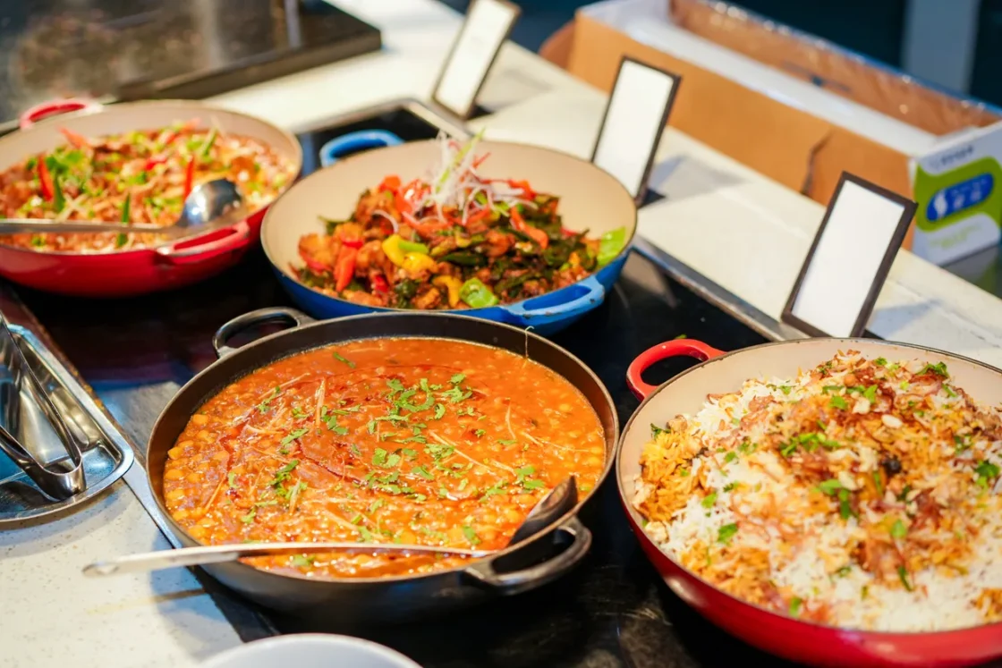 Multiple professional-grade cooking pans with prepared dishes including stir-fried vegetables, rice, and sauces for wholesale food service and bulk meal preparation.