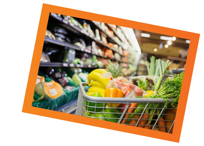 Shopping cart filled with fresh fruits and vegetables in a vibrant grocery store.