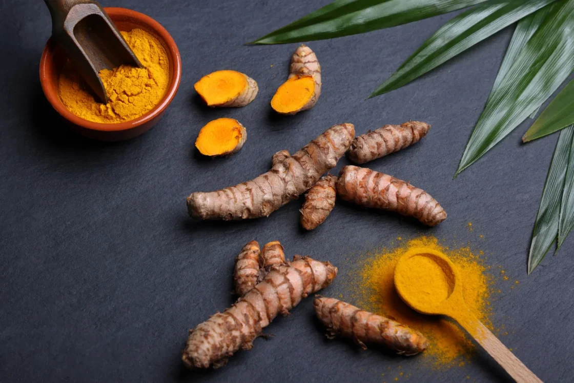 Fresh turmeric and ginger root displayed with ground turmeric powder in bowls, ideal for wholesale food suppliers and distributors.